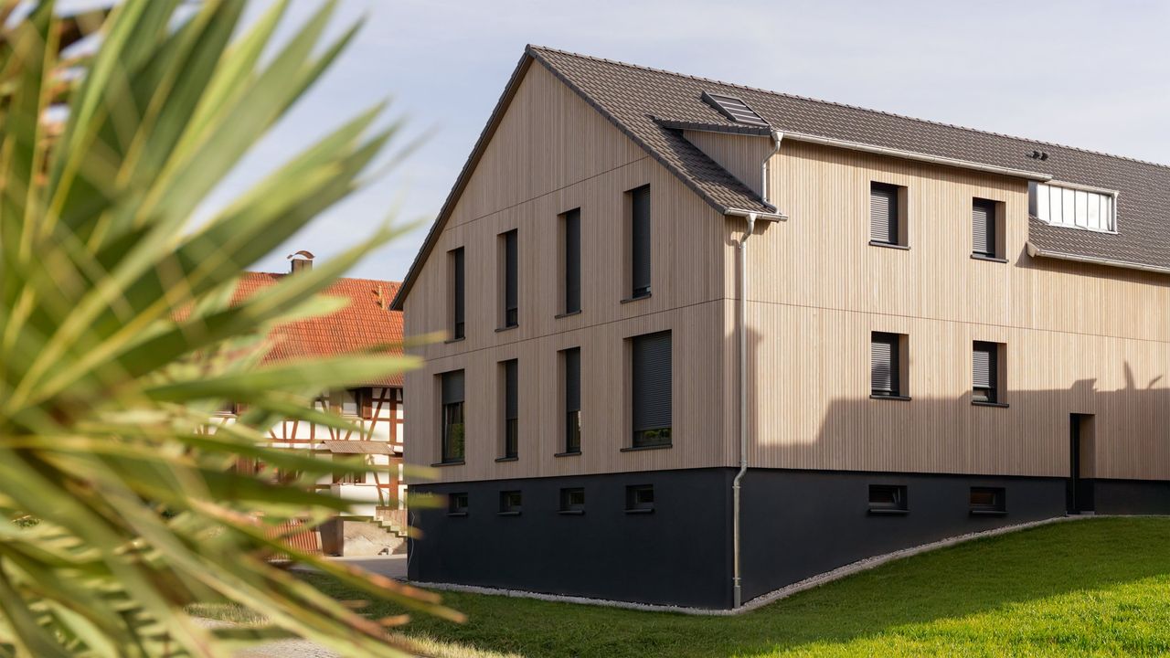 Wohnhaus mit heller Holzfassade und dunklem Sockel, Außenaufnahme